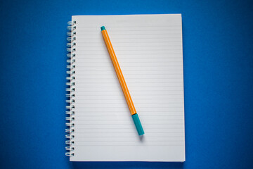 Flat lay of notepad and yellow pen on blue background