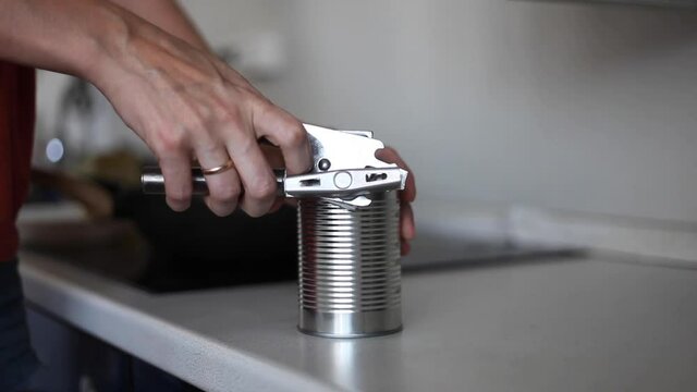A woman in the kitchen opens a can. Hand open canned food in metal can. Close up canned goods non perishable food storage goods in kitchen home