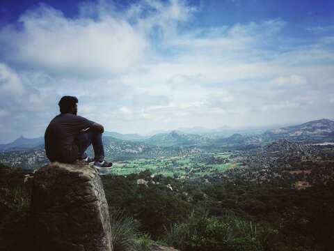 A teenager sitting atop a rock on a hill and admiring the beauty of nature. 
