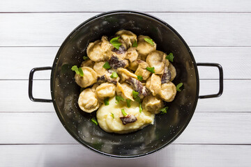 Russian food pelmeni, meat dumplings with mushroom sauce and mashed potatoes in black bowl. Close-up, top view