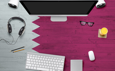 Qatar flag background with headphone,computer keyboard and mouse on national office desk table.Top view with copy space.Flat Lay.
