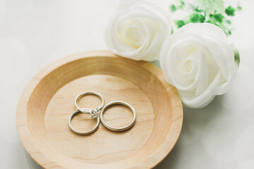 白バラが添えられた小皿に置かれた婚約指輪と結婚指輪