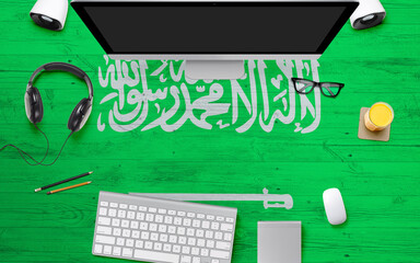Saudi Arabia flag background with headphone,computer keyboard and mouse on national office desk table.Top view with copy space.Flat Lay.