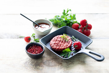 Raw burger cutlets with salt, pepper, herbs and spice for grilling on a wooden table.
