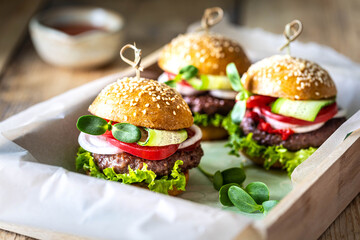 Group of burgers with tomato sauce on a wooden tray.