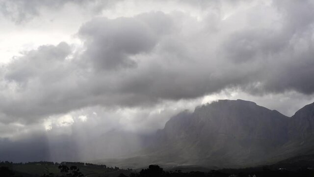 A time-lapse of a storm moving in over the mountains with building clouds and light rays beaming through the clouds