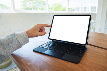 Mockup image of a woman using and pointing finger at tablet pc with blank desktop white screen as a computer pc on wooden table
