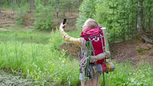 Woman with backpack walking in a forest and take a selfie with a mobile phone.