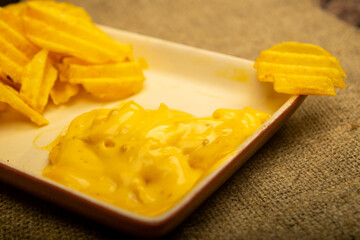 Potato chips with cheese sauce on a wooden background. Close up.