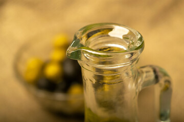 The neck of a glass bottle for olive oil against a background of green olives, black olives and...