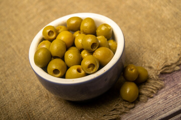 Green olives in a ceramic bowl on a background of coarse-textured burlap. Close up.