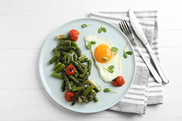 Oven baked asparagus served with fried egg on white wooden table, flat lay