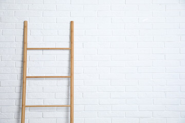 Modern wooden ladder near white brick wall. Space for text