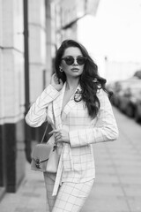 Young beautiful elegant woman in white casual costume walking at street on a summer day. Pretty lady wearing sunglasses and holding handbag. Businesswoman standing and posing in the city