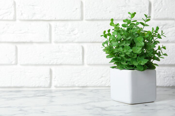 Beautiful artificial plant in flower pot on white marble table near brick wall. Space for text