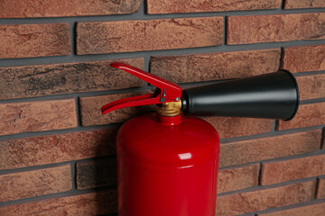 Naklejka premium Fire extinguisher near brick wall, closeup view