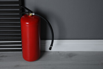 Fire extinguisher near grey wall indoors. Space for text