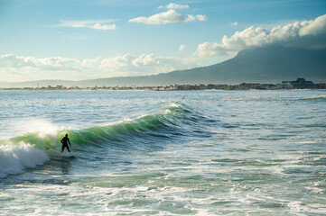 A surfer on a wave in with a mountain and coastline behind a wave.  - 363825127