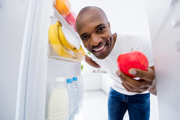 Close-up portrait of his he nice attractive cheerful cheery guy looking in fridge taking red ripe...