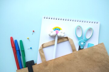 Various Colorful stationery for creativity (Scissors, markers, paints, brushes, pencils, colored paper) in paper bag on blue background.Stationery delivery.Contactless delivery. Back to school concept