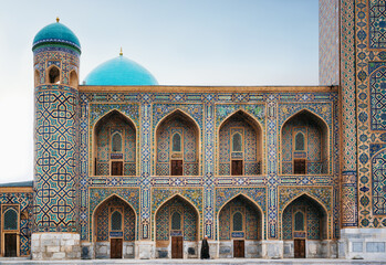 Man in black wear walks along Tilya-Kori madrasah in Registan, Samarqand, Uzbekistan