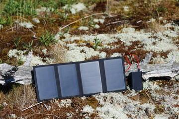 Tourist solar panel and power bank in forest are charging. Camping equipment, alternative power source.