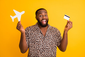 Close-up portrait of his he nice attractive handsome cheerful cheery guy holding in hands paper aircraft bank card purchase pay tour isolated over bright vivid shine vibrant yellow color background