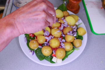 A hand throws salt on a newly- boiled potatoes on a plate with spinach and onions and cheese.