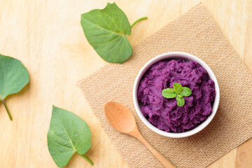Obraz na płótnie Canvas Mashed purple sweet potatoes in a bowl and spoon on wooden background, Healthy food 