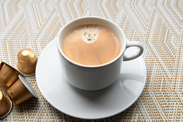 Close up golden capsules or pods for coffee mashine with cup on gold and white background. 