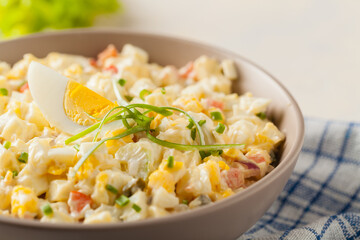 A light egg salad with celery, gherkin, pepper and mayonnaise. Served in a bowl on a light background. Front view.