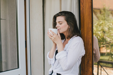 Young beautiful woman drinking tea on cozy terrace of a wooden country house.