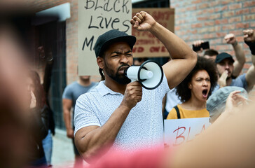 African American man shouting through megaphone while protesting with crowd of people on the...