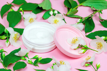 Obraz na płótnie Canvas White plastic cosmetic container for moisturizing cream as a mock up with bright fresh jasmine flowers on light pink background. Body and skin care, health, wellness and beauty concept.