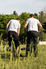 Two friends standing on their green bikes in a park, talking and examining them. Day filled with sun and sports activity. Mates having fun in the park.