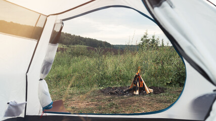 View through a tent on a bonfire on a background of nature. The concept of local travel, tourism and camping. Copy space.