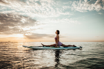Young woman doing YOGA on a SUP board in the lake at sunrise