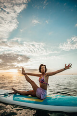Fototapeta na wymiar Young woman doing YOGA on a SUP board in the lake at sunrise