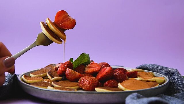 Pouring honey or maple syrup on trendy tiny pancakes with strawberry and mint leaf. trendy quarantine food. Slow motion honey or maple syrup pours. Plate with mini pancakes