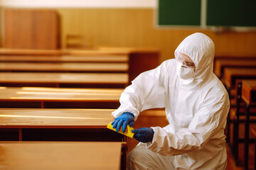 Man in a protective suit washes school desk. Cleaning and disinfection school class to prevent...