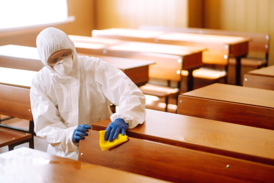 Man in a protective suit washes school desk. Cleaning and disinfection school class to prevent COVID-19.