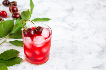 Cherry cold drink in a glass cup, cherry berries and green leaves on a white background. A refreshing fruit summer compote.