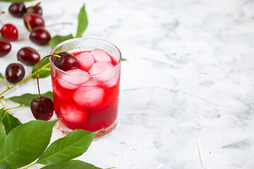 Cold drink in a glass cup with ice, cherry berries and green leaves on a white background. Refreshing fruit summer sangria (punch).