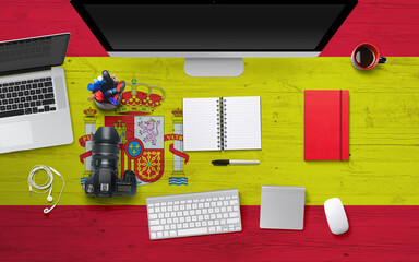 Spain flag background with headphone,camera, notebook and mouse on national office desk table.Top view with copy space.Flat Lay.