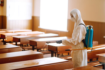 Disinfecting school class to prevent COVID-19. Man in protective hazmat suit with spray chemicals to preventing the spread of coronavirus, pandemic in quarantine city. 