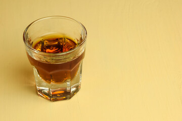 A glass of cognac stands on a beige table. Shot from above