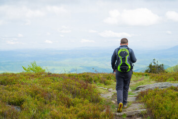 Man heading from the mountain by the rocky trail. The guy in gray training clothes and a green backpack