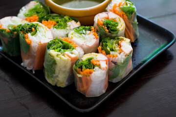 Portion of spring rolls on old wood with spicy sauce, vegetables and in noodle tube