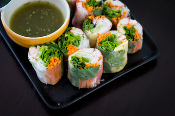 Portion of spring rolls on old wood with spicy sauce, vegetables and in noodle tube