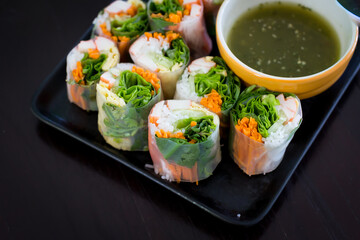 Portion of spring rolls on old wood with spicy sauce, vegetables and in noodle tube